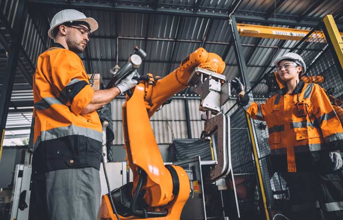 Engineer team service robot welding working in automation factory. People worker in safety suit work robotic arm software programming or replacing part in automated manufacturing industry technology.